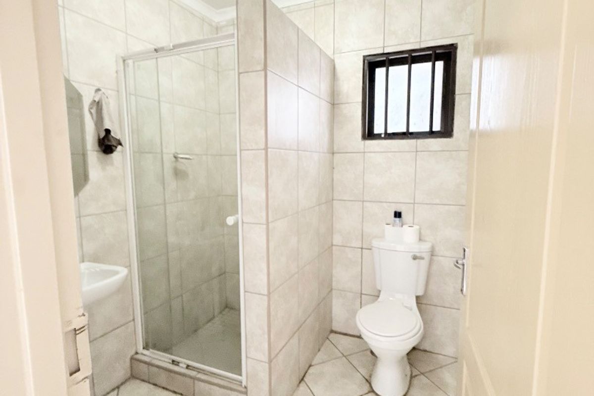 A functional bathroom featuring a tiled shower enclosure, toilet, and wall-mounted basin with neutral wall and floor tiles.