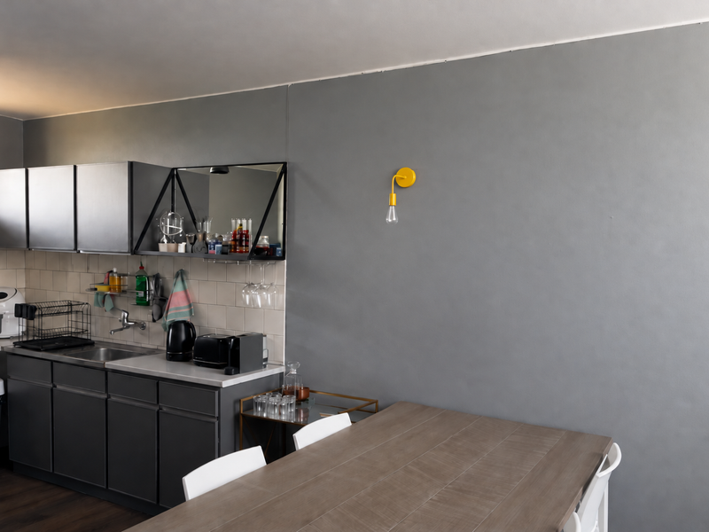 A modern kitchen area featuring dark grey cabinetry, a tiled backsplash, and a functional sink, seamlessly integrated into an open-plan living space.