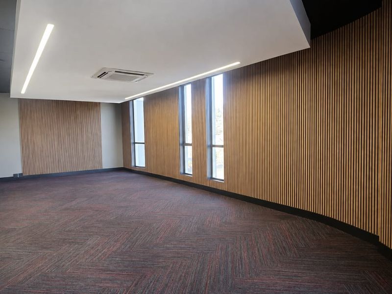 A modern, empty office space featuring contemporary timber slat wall paneling, recessed linear lighting, a cassette air conditioning unit, and carpeted flooring.