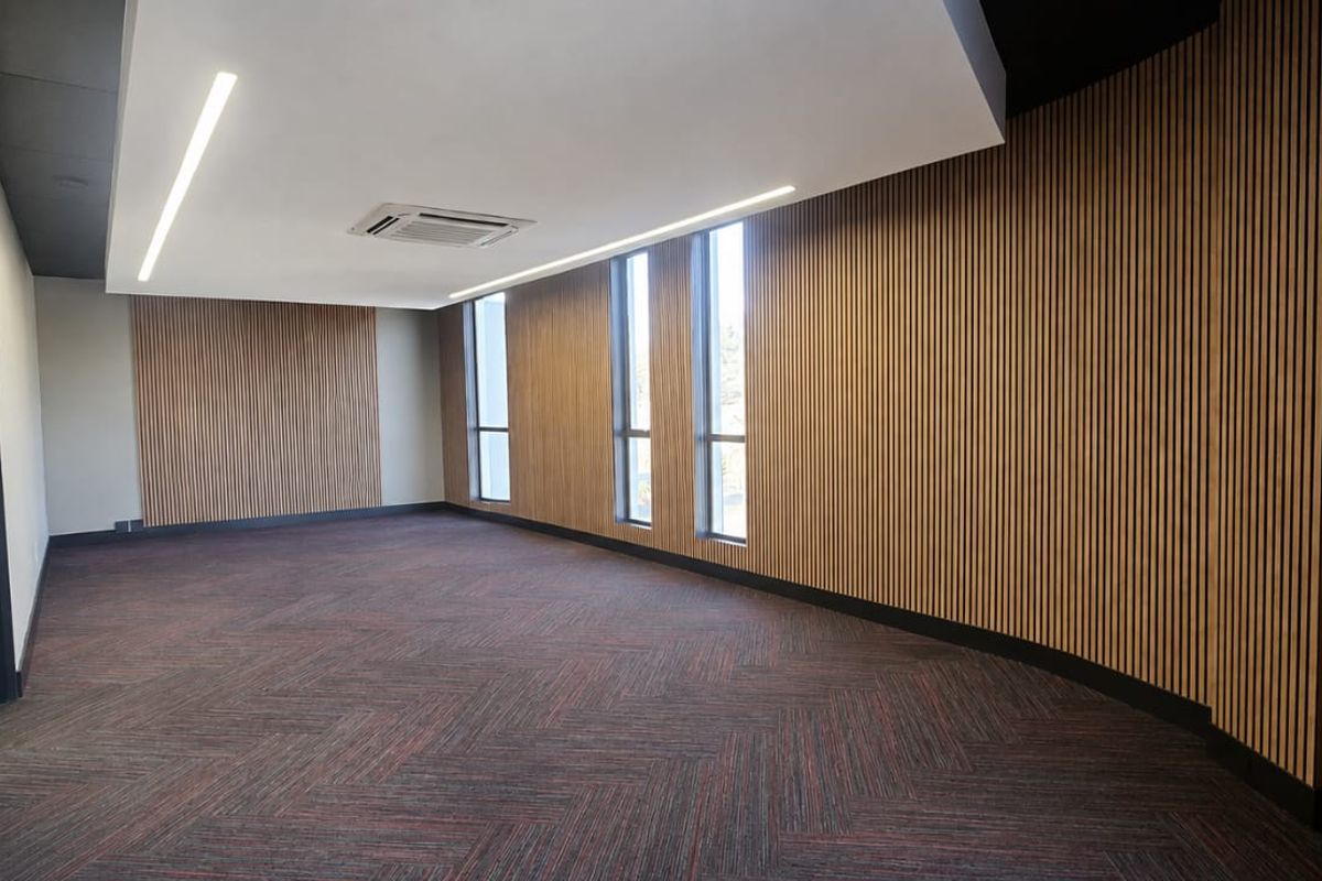 A modern, empty office space featuring contemporary timber slat wall paneling, recessed linear lighting, a cassette air conditioning unit, and carpeted flooring.