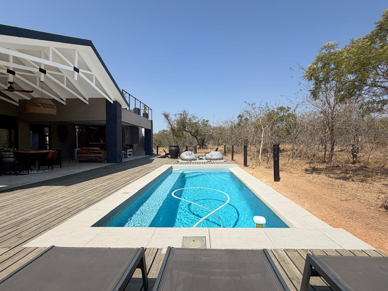 Outdoor entertainment area featuring a swimming pool with stone coping, surrounded by timber decking and a spacious covered patio with exposed roof trusses.
