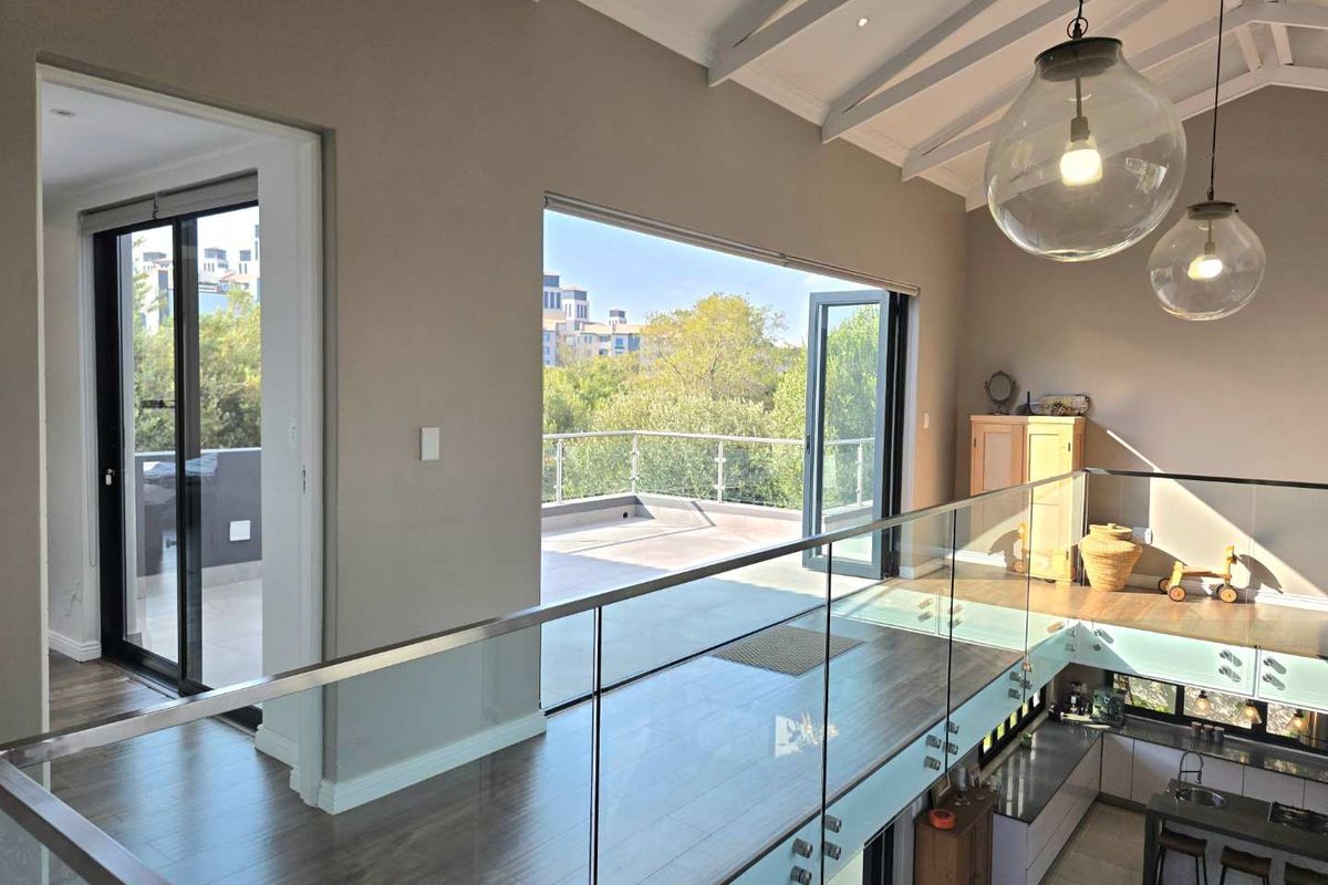 Spacious mezzanine living area featuring vaulted ceilings, glass balustrades, and seamless access to an outdoor balcony with elevated views.