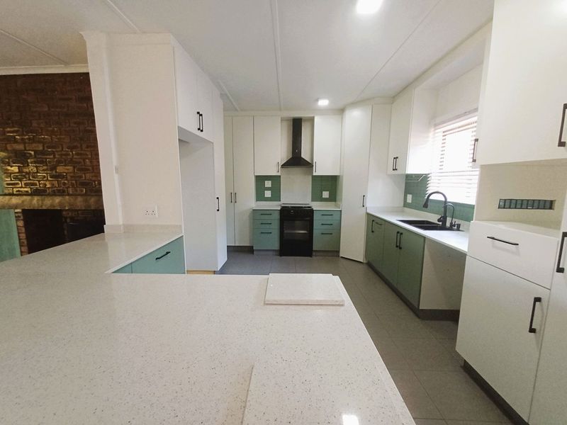 Modern kitchen featuring white and sage green cabinetry, quartz countertops, a built-in stove with extractor fan, and a sleek tiled backsplash.