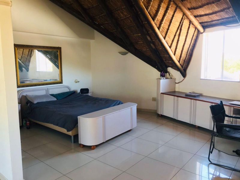 Spacious bedroom featuring a unique vaulted thatched roof with exposed timber rafters, tiled flooring, and built-in storage cabinetry.