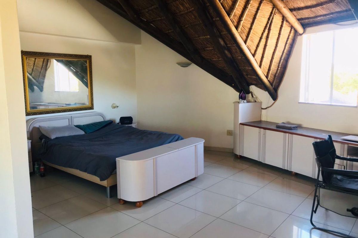 Spacious bedroom featuring a unique vaulted thatched roof with exposed timber rafters, tiled flooring, and built-in storage cabinetry.