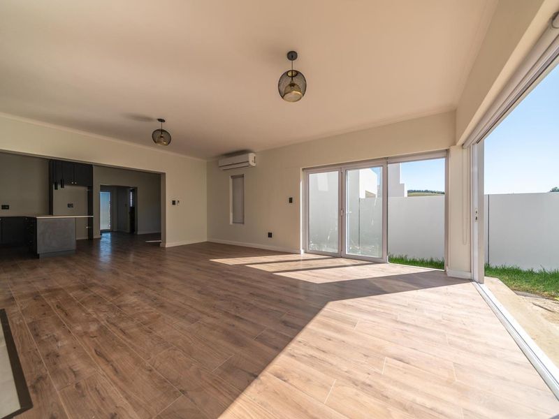 Spacious open-plan living area featuring wood-look tile flooring, modern pendant lighting, and large sliding glass doors opening to the exterior.