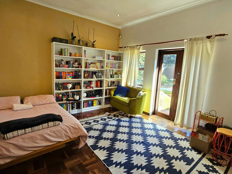 Spacious bedroom featuring warm parquet flooring, built-in shelving, and direct access to the garden through a glass panel door.