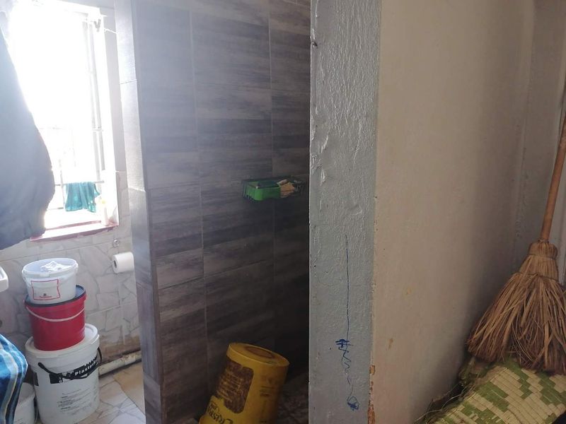 A small bathroom space featuring tiled shower walls and a window with security bars, currently requiring cosmetic updates and wall repairs.