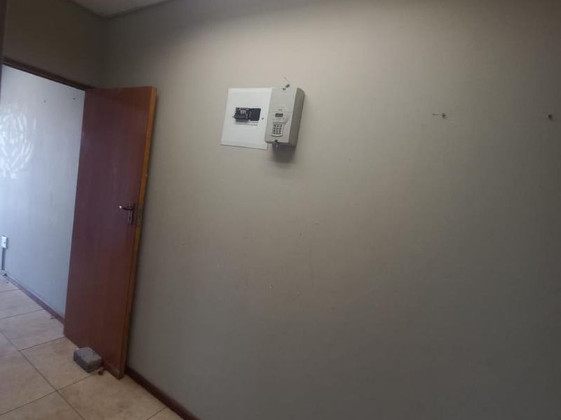 A vacant commercial hallway featuring tiled flooring, a drop ceiling with integrated lighting, and a wall-mounted security alarm keypad.