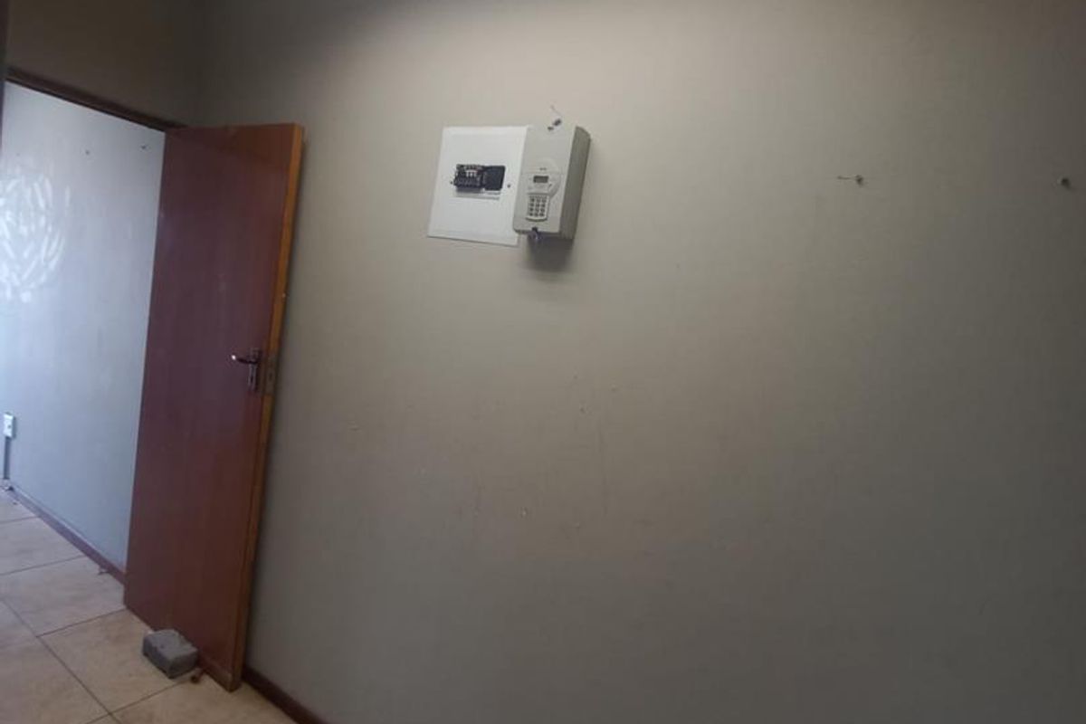 A vacant commercial hallway featuring tiled flooring, a drop ceiling with integrated lighting, and a wall-mounted security alarm keypad.