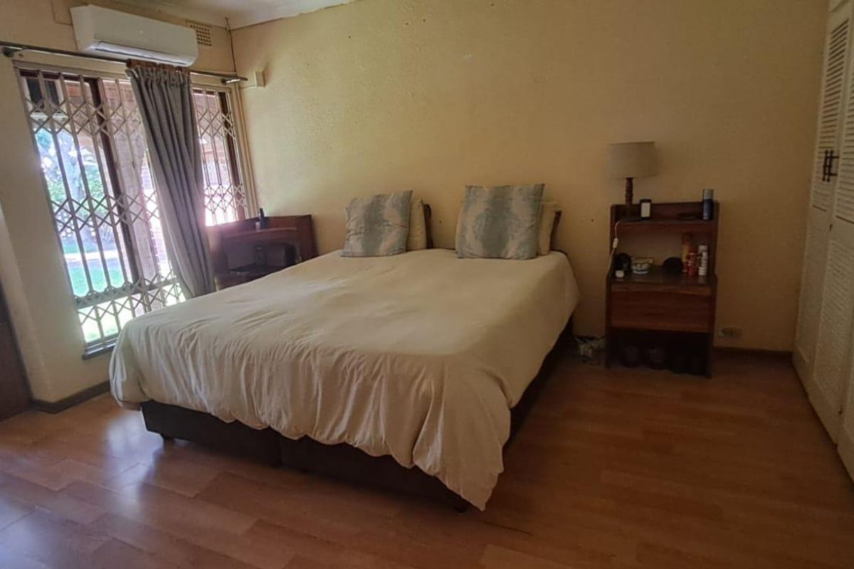 Spacious bedroom featuring built-in cupboards, laminate flooring, and a wall-mounted air conditioning unit.