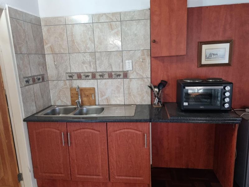 A compact kitchen area featuring laminate cabinetry, granite countertops, a double sink, and a tiled backsplash, providing a functional prep space.
