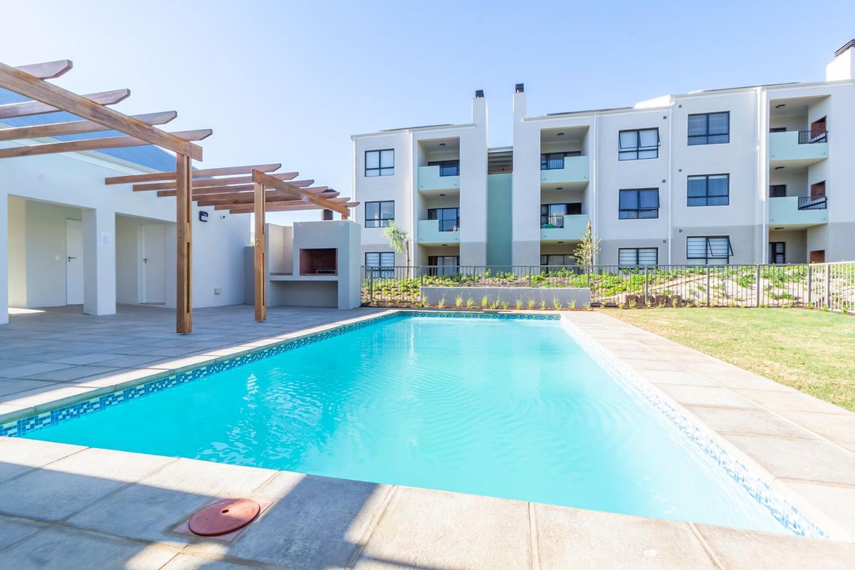 Communal pool area featuring a paved deck, timber pergola, and built-in braai facility, set within a well-maintained apartment complex.