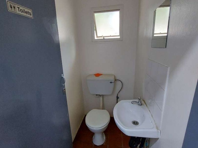 A compact, functional guest bathroom featuring a toilet, wall-mounted basin, and tiled flooring, suitable for a small apartment or utility area.