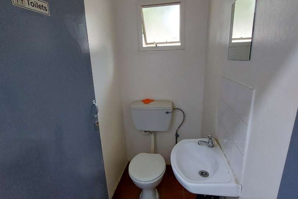 A compact, functional guest bathroom featuring a toilet, wall-mounted basin, and tiled flooring, suitable for a small apartment or utility area.