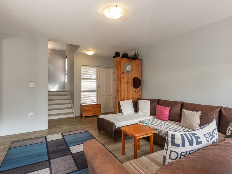 A living room area featuring laminate flooring, a staircase leading to the upper level, and neutral wall finishes.