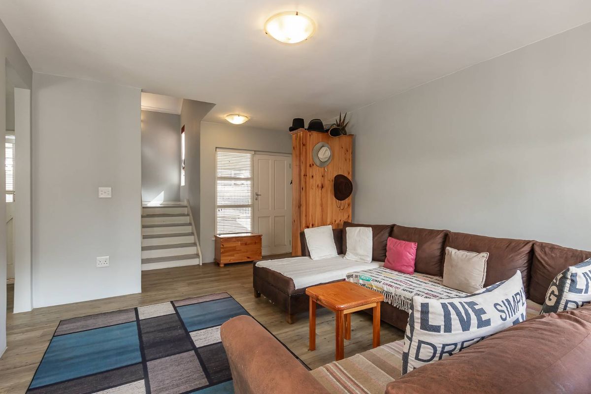 A living room area featuring laminate flooring, a staircase leading to the upper level, and neutral wall finishes.