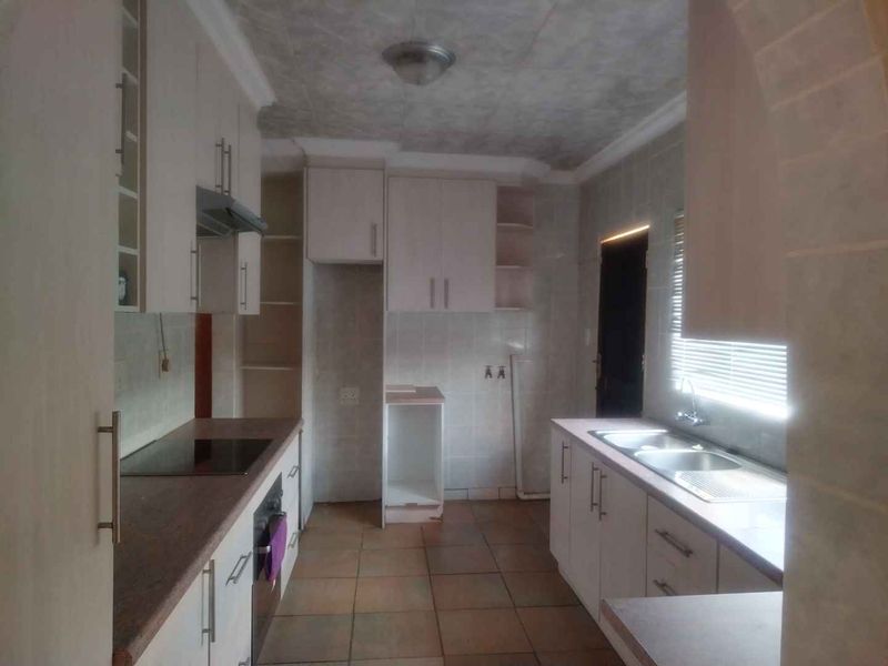 A functional kitchen featuring built-in cabinetry, laminate countertops, an electric hob, oven, extractor fan, and a double bowl sink with tiled flooring.