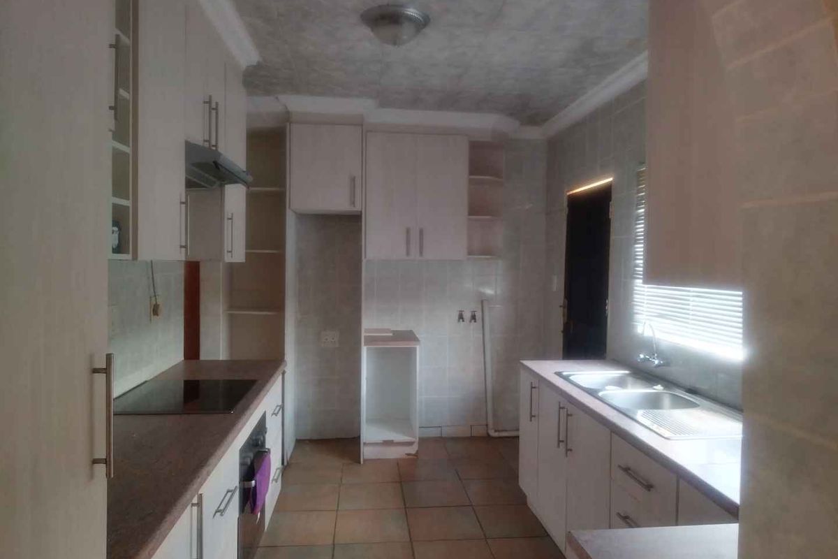 A functional kitchen featuring built-in cabinetry, laminate countertops, an electric hob, oven, extractor fan, and a double bowl sink with tiled flooring.