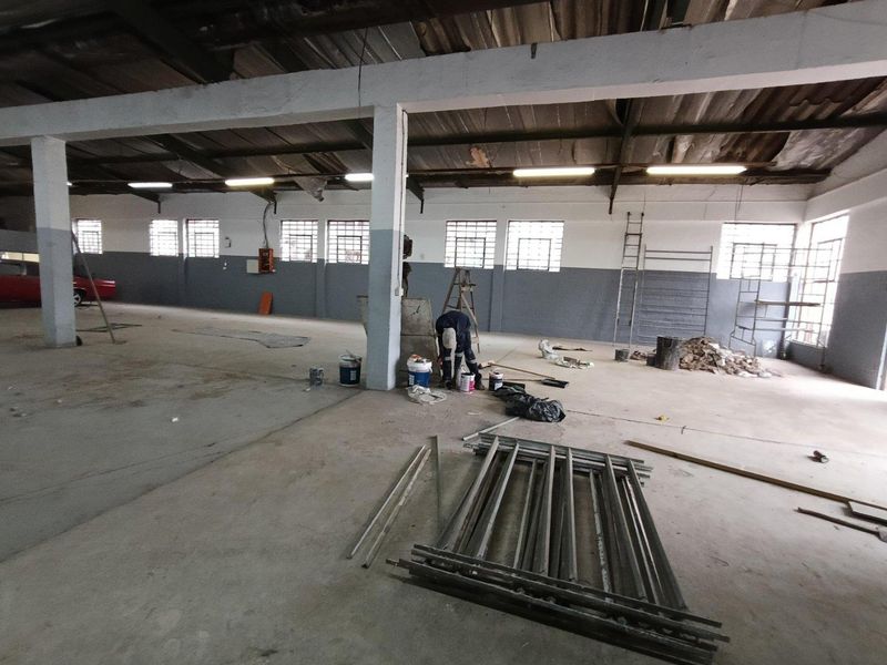 Spacious industrial warehouse area featuring high ceilings, concrete flooring, and large windows, currently undergoing maintenance and renovation.