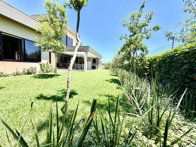 A well-maintained rear garden featuring a lush lawn, established perimeter landscaping, and a covered patio area accessible via large sliding glass doors.