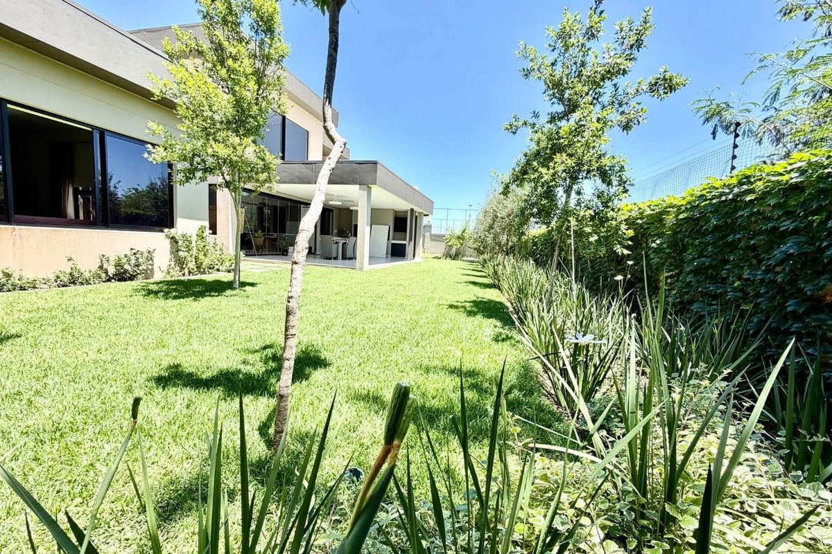 A well-maintained rear garden featuring a lush lawn, established perimeter landscaping, and a covered patio area accessible via large sliding glass doors.
