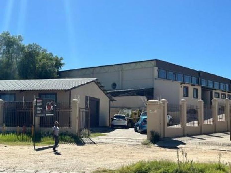 Front exterior view of an industrial property featuring a metal-roofed building, secure perimeter fencing, and a gated entrance.