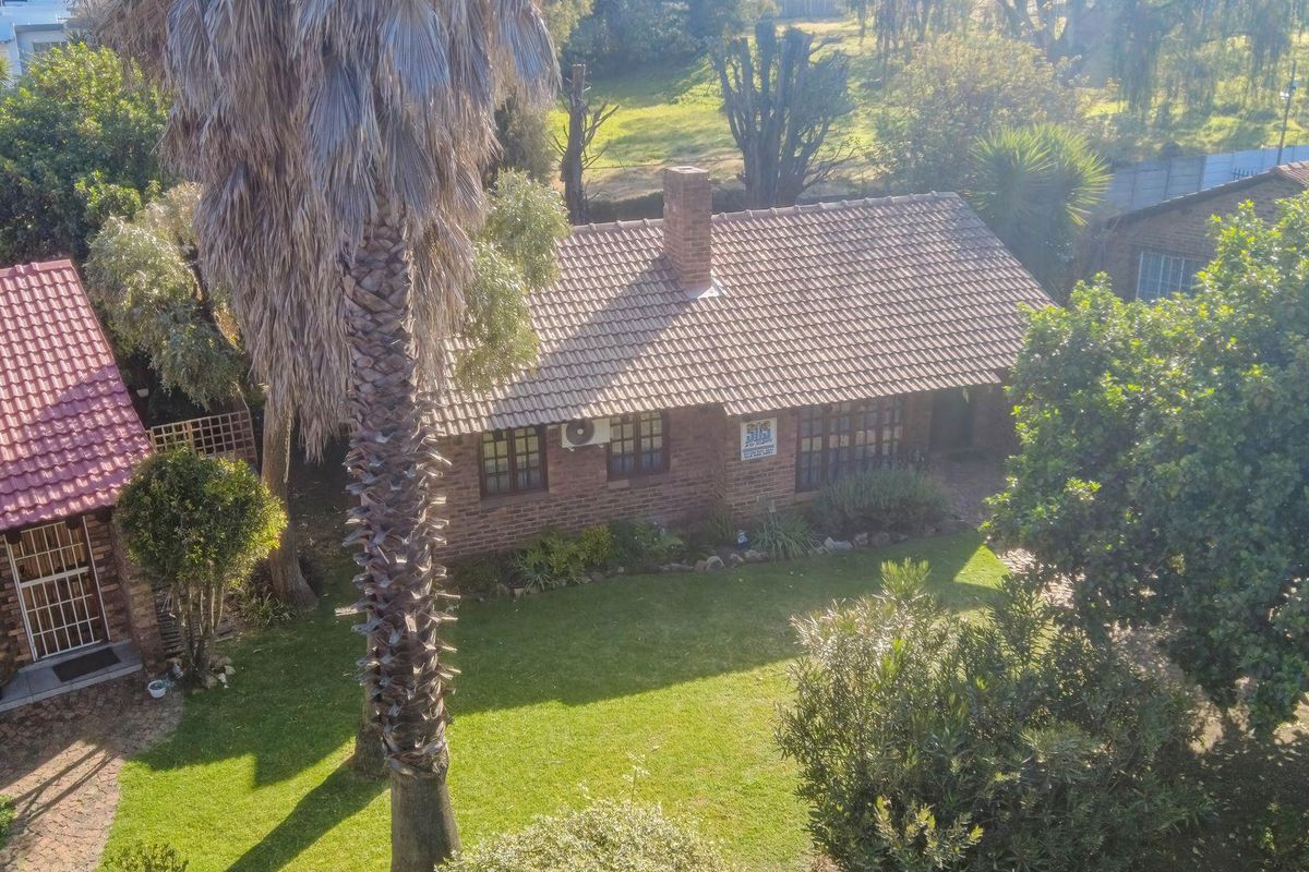 Aerial view of a brick townhouse featuring a tiled roof, chimney, and established garden with mature trees.