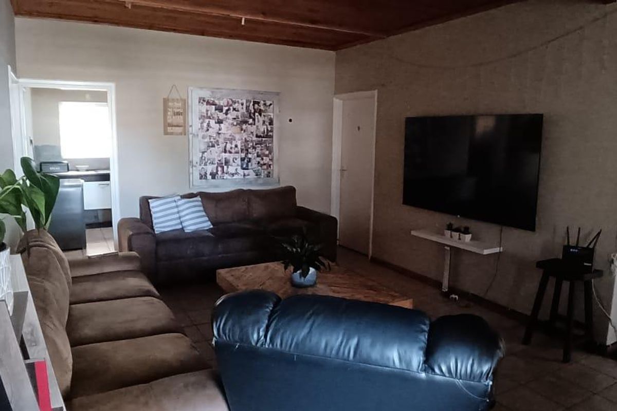 A living room featuring tiled flooring and a timber-paneled ceiling, with an open-plan layout leading to an adjacent kitchen area.