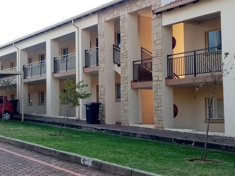 Exterior view of a multi-story apartment complex featuring stone-clad pillars, private balconies with metal railings, and a paved ground-level walkway.