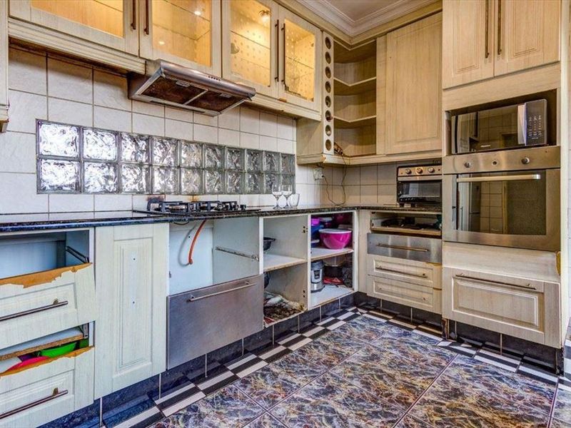 A dated kitchen featuring built-in cabinetry, granite countertops, and integrated appliances, currently showing significant wear and missing cabinet components.