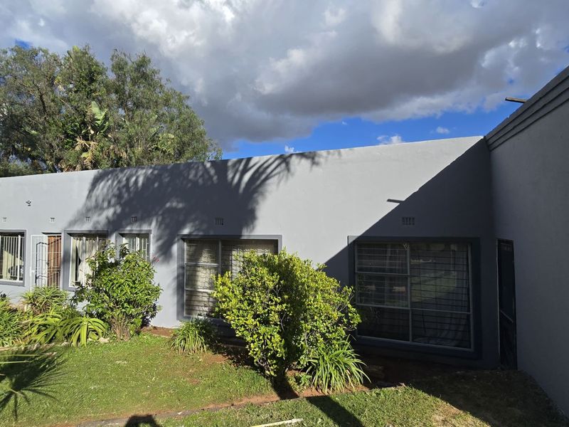Rear elevation of the house featuring grey painted exterior walls, aluminium window frames with security bars, and a landscaped garden area.