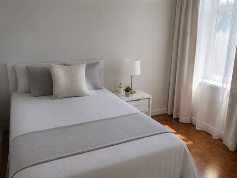 A bright and well-maintained bedroom featuring warm parquet flooring and neutral wall finishes, complemented by natural light from the window.