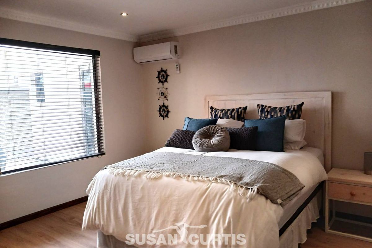 A well-maintained bedroom featuring light wood-look flooring, recessed ceiling lighting, and a wall-mounted air conditioning unit.
