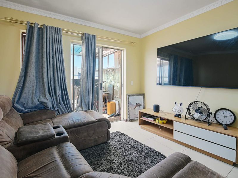 A comfortable living room featuring tiled flooring, crown molding, and a sliding glass door providing access to an outdoor balcony area.