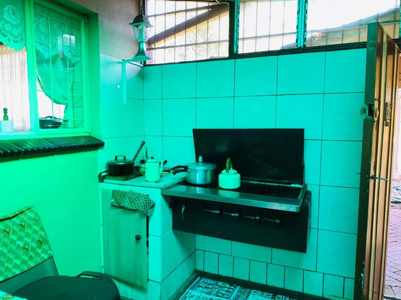 A functional scullery or prep area featuring built-in stove, tiled splashbacks, and fixed cabinetry, requiring cosmetic updates to modernize the space.