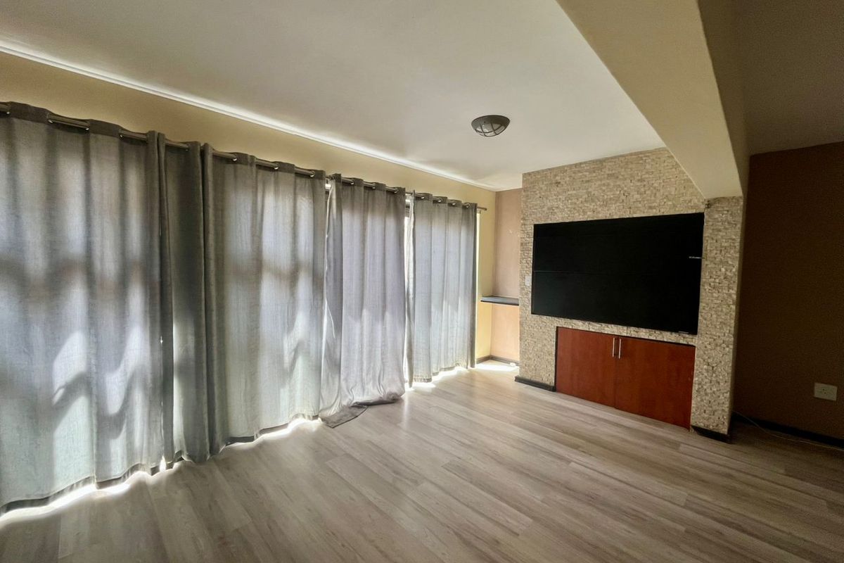 A living room featuring light wood-look laminate flooring, a stone-clad feature wall with built-in cabinetry, and floor-to-ceiling curtains.