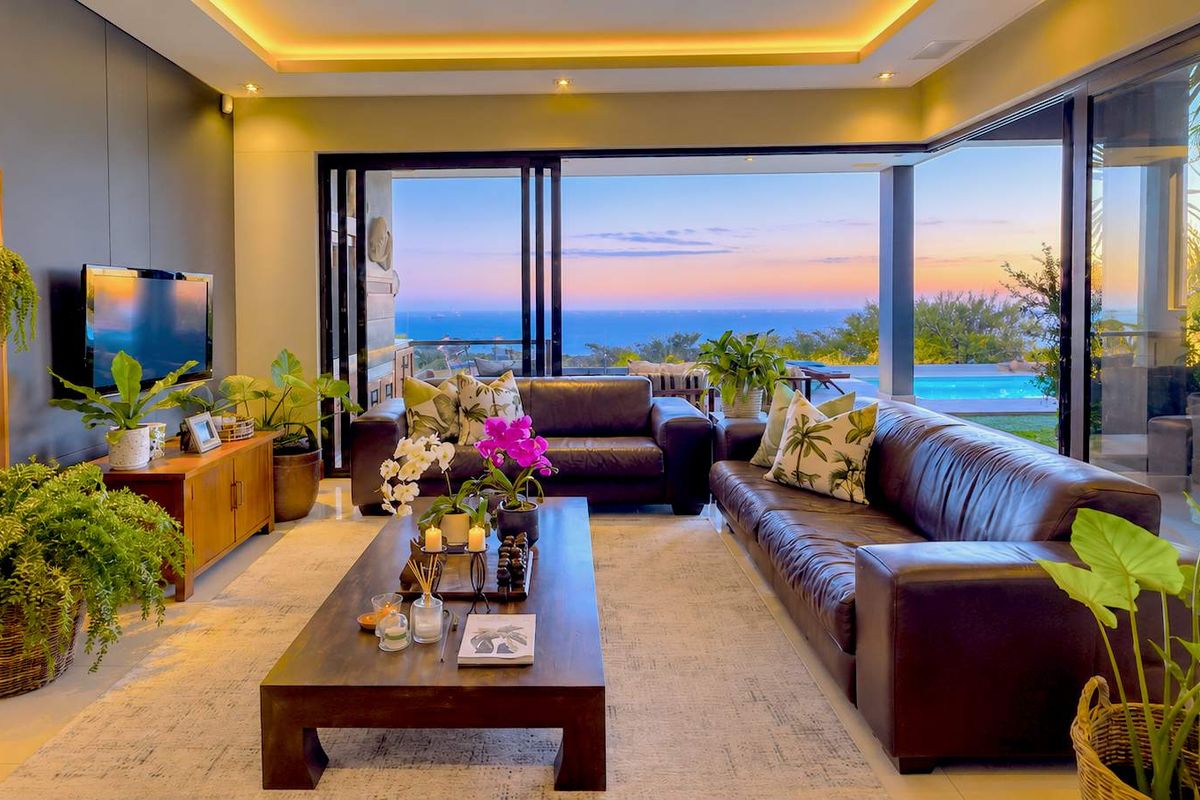 Modern living room featuring recessed cove lighting, large sliding glass doors, and seamless indoor-outdoor flow with expansive ocean views.