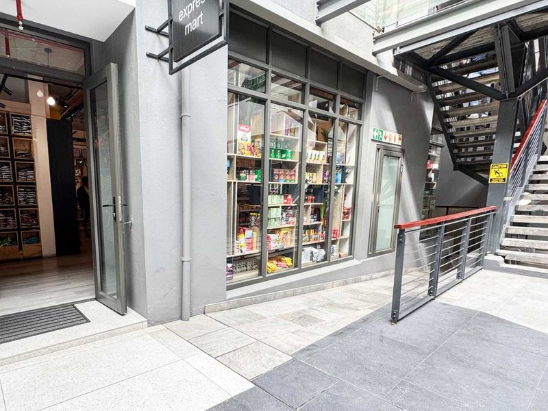 A modern retail storefront featuring a glass display window, metal staircase access, and clean tiled exterior flooring in a commercial complex.