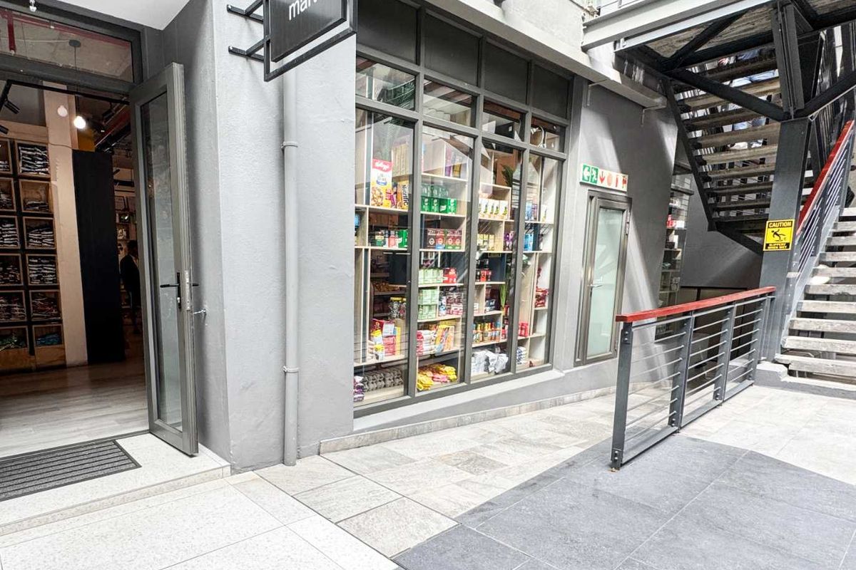 A modern retail storefront featuring a glass display window, metal staircase access, and clean tiled exterior flooring in a commercial complex.