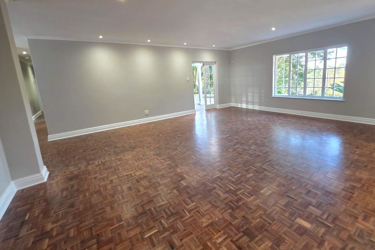 Spacious living area featuring polished parquet timber flooring, recessed downlighting, and large windows providing natural light with access to an outdoor area.