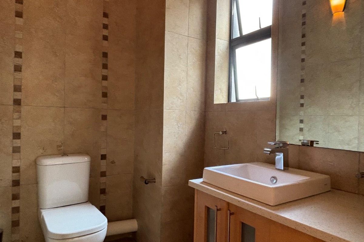 A functional bathroom featuring a modern vessel sink vanity, wall-mounted mirror, and a standard toilet with neutral floor-to-ceiling wall tiling.