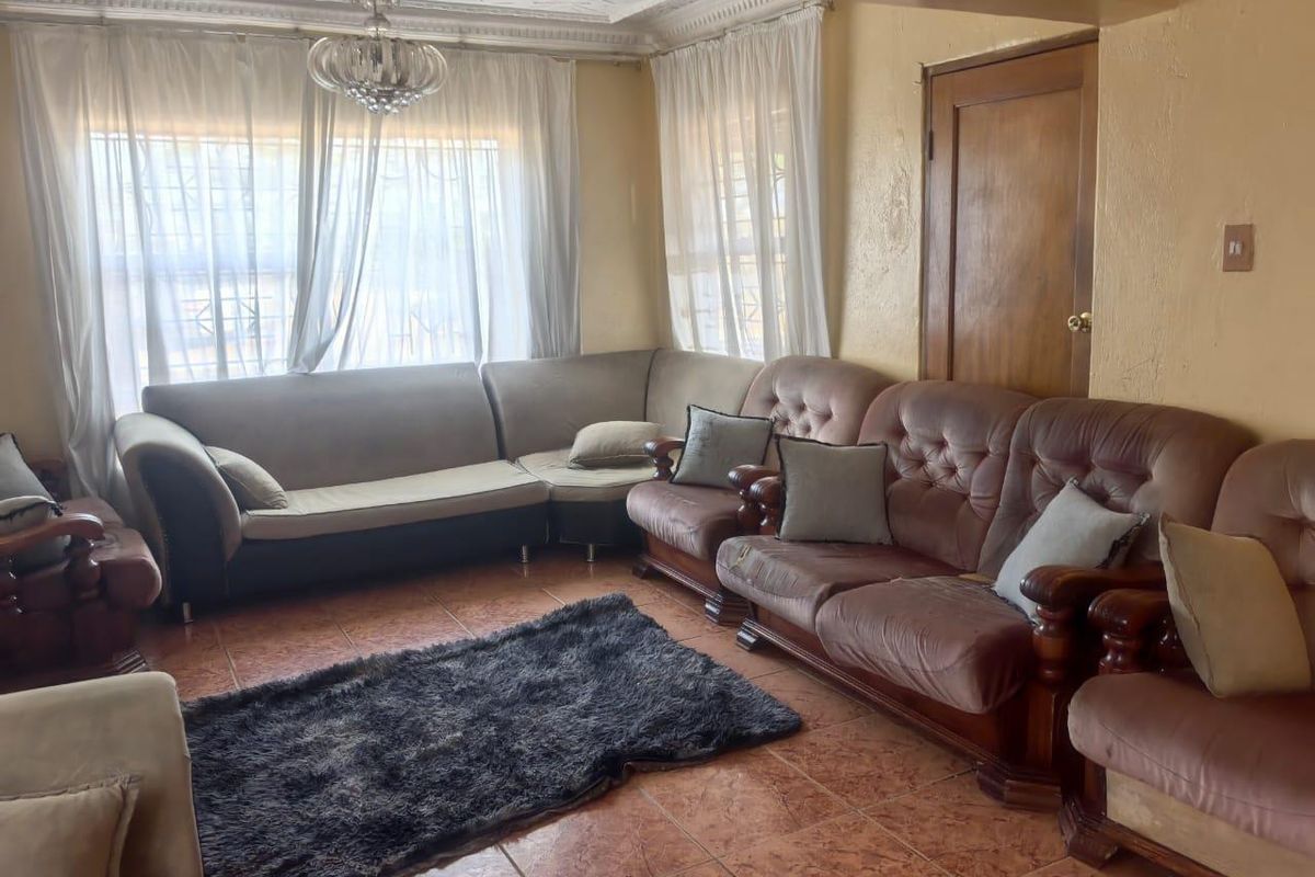 A living room featuring tiled flooring, decorative ceiling molding, and a central chandelier, providing a functional space for relaxation.