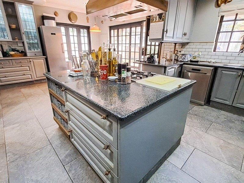 Spacious kitchen featuring a central island with granite countertops, gas hob, extractor fan, subway tile backsplash, and ample built-in cabinetry with stone flooring.