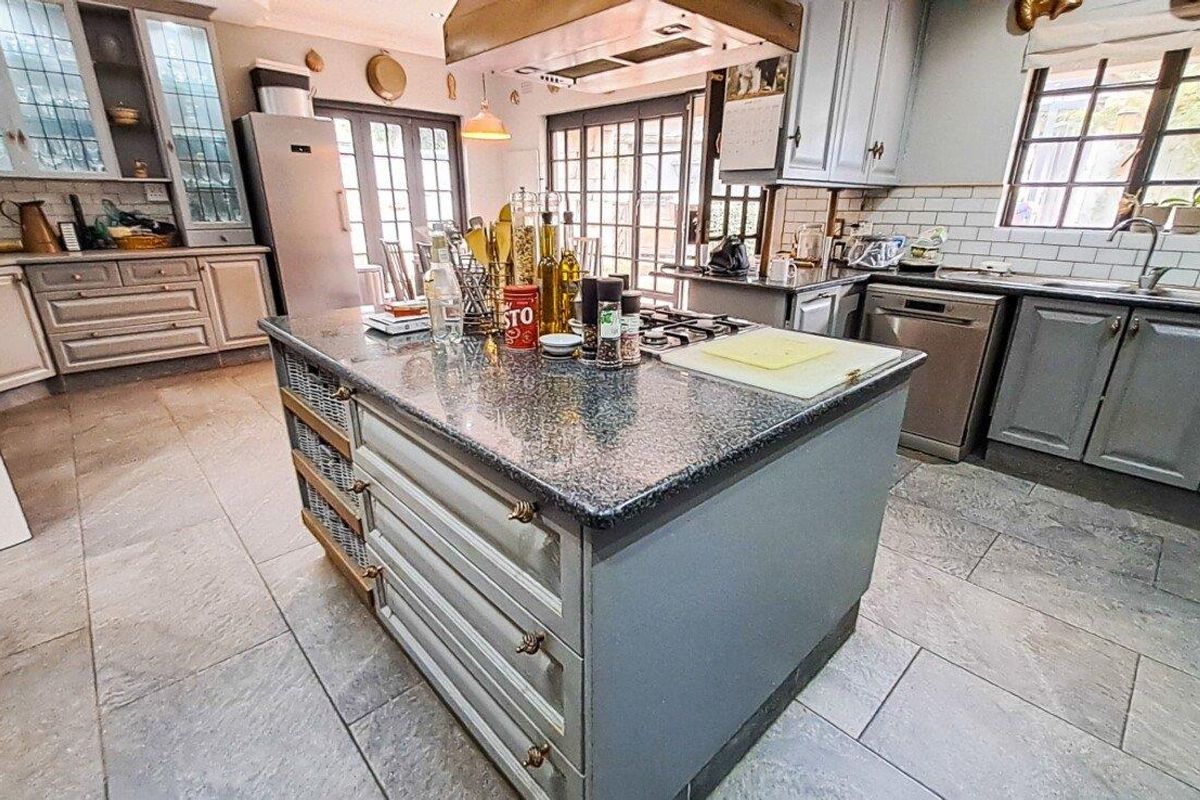 Spacious kitchen featuring a central island with granite countertops, gas hob, extractor fan, subway tile backsplash, and ample built-in cabinetry with stone flooring.