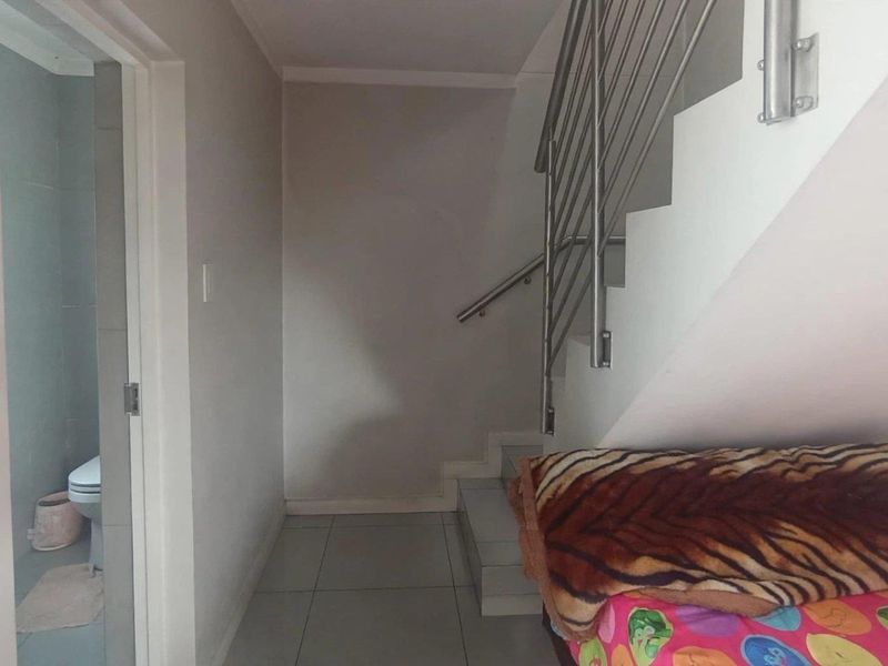 A functional hallway featuring a staircase with a stainless steel balustrade, tiled flooring, and access to an adjacent bathroom.