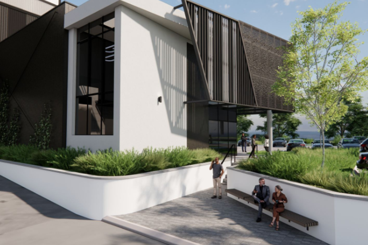 Modern industrial building exterior featuring decorative metal screening, large glass windows, and a landscaped paved entrance area with integrated seating.