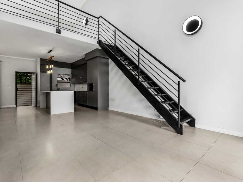Modern open-plan living area featuring a sleek kitchen with island, tiled floors, and a striking staircase leading to an upper level.
