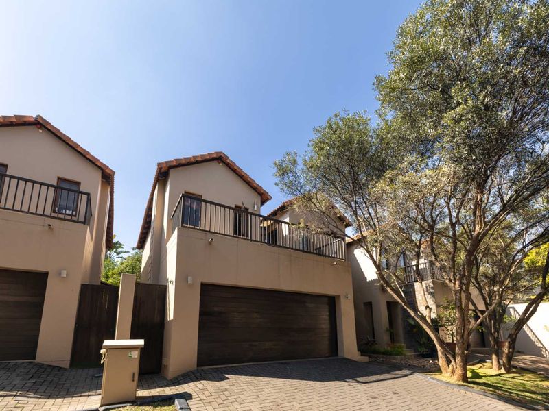 Front exterior view of a townhouse complex featuring paved driveways, double garages, and upper-level balconies with metal railings.