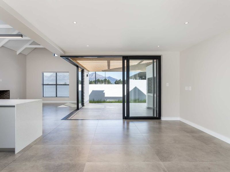 Spacious open-plan living area featuring large sliding glass doors that open onto a covered patio, with modern tiled floors and recessed lighting.